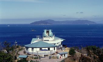 a large building with a blue roof is situated on a hill overlooking the ocean at Daiwa Roynet Hotel Oita