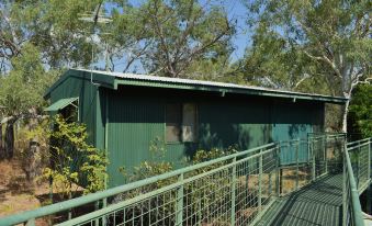 a green building with a metal railing is surrounded by trees and bushes , under a clear blue sky at Parry Creek Farm Tourist Resort & Caravan Park