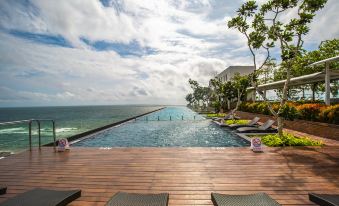 a large pool is surrounded by lounge chairs and a wooden deck with an ocean view at Marino Beach Colombo