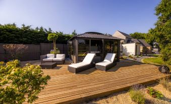 a wooden deck with a gazebo , lounge chairs , and umbrellas , surrounded by a garden and trees at La Ramade - Teritoria