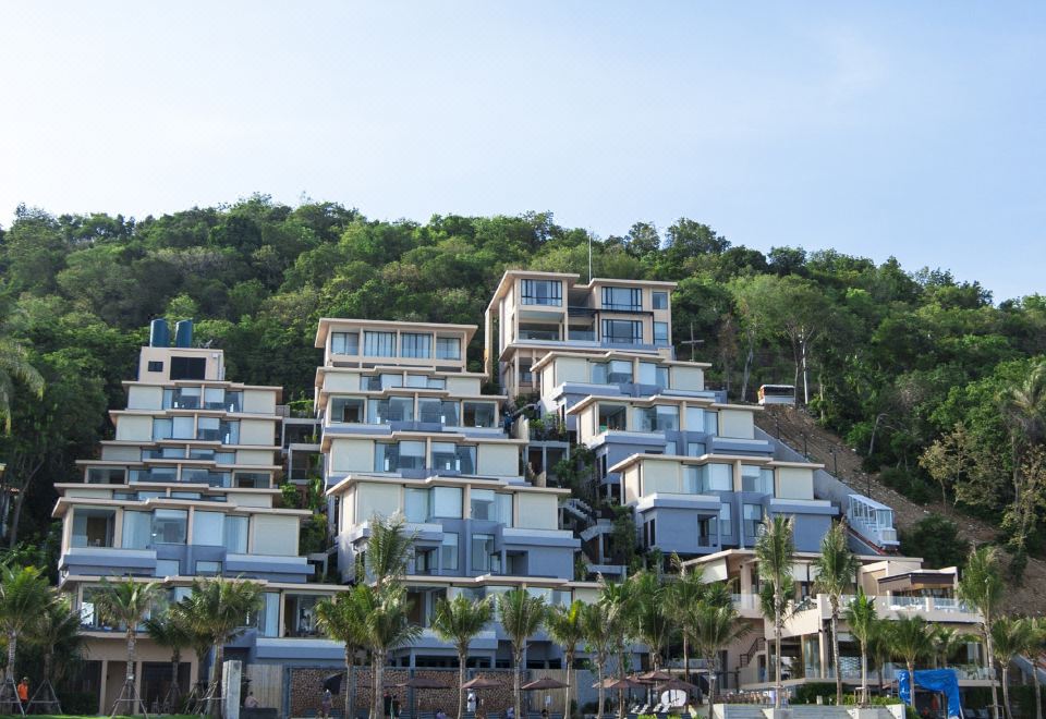 a beach resort on a hillside , with multiple buildings and trees surrounding the area , set against the backdrop of clear blue skies at Bandara Villas, Phuket