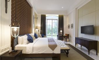 a spacious bedroom with a king - sized bed , a large flat - screen tv mounted on the wall , and a comfortable seating area at Plataran Heritage Borobudur Hotel