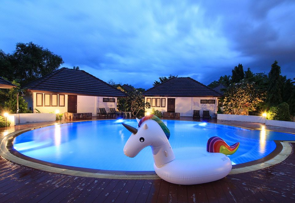 a large outdoor swimming pool surrounded by grass , with a white inflatable unicorn floating in the water at Baan Suan Nuanta