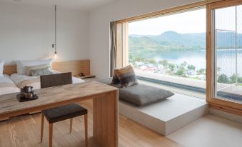 a modern bedroom with a large window offering a view of the water , wooden flooring , and minimalist furniture at WE Hotel Toya