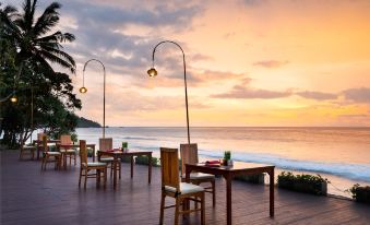 a beautiful sunset over the ocean , with wooden tables and chairs set up on a wooden deck overlooking the water at Holiday Resort Lombok