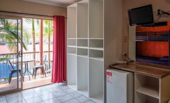 a room with a television , bookshelves , and a door leading to a balcony overlooking trees at Brisbane Backpackers Resort