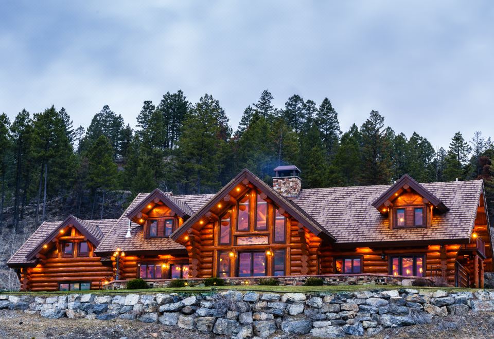 a large , log cabin - style house with a stone wall and several trees in the background at Coyote Bluff Estate