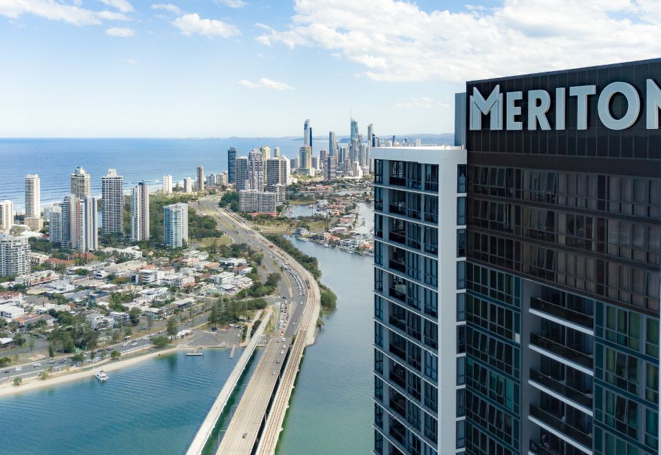 a city skyline with a tall building and a body of water in the background at Meriton Suites Southport