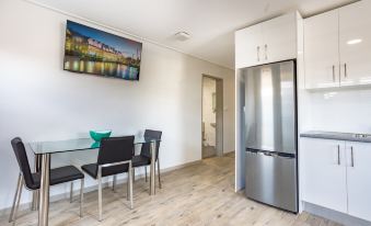 a modern kitchen with a stainless steel refrigerator , black chairs , and a glass dining table at Hamilton on Beaumont