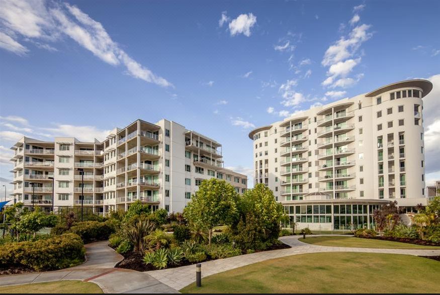 a modern apartment building surrounded by a park , with a clear blue sky in the background at Bunbury Hotel Koombana Bay