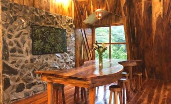 a wooden dining table surrounded by chairs , situated in a room with stone walls and large windows at Volcano House