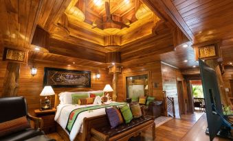 a bedroom with wooden walls and ceiling , a bed , couch , and lamp , all decorated in a rustic style at Khum Wang Nuea Villa