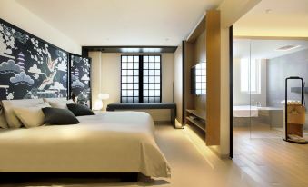 A modern bedroom with large windows and a white bed in the middle, accompanied by an open space at Ginco Hotel