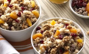 two white bowls filled with oatmeal topped with granola and fruit , placed on a wooden table at Home2 Suites by Hilton Gonzales