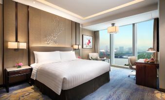 The bedroom features large windows and a balcony that overlook the city, with an elegant bed positioned in front at Shangri-La Hotel, Yiwu