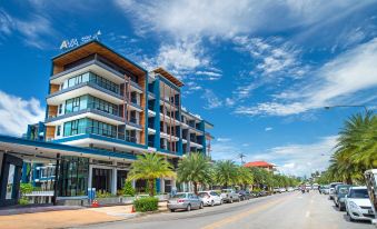 a large blue building with multiple floors , surrounded by palm trees and a street with cars parked on the side at AVA SEA Resort Krabi