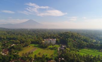a large , white building surrounded by lush greenery and a tennis court in the distance at Plataran Heritage Borobudur Hotel