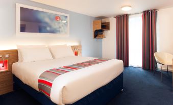 a large bed with white linens and a blue base is in a room with blue carpet , white curtains , and a painting on the wall at Travelodge Norwich Central Riverside