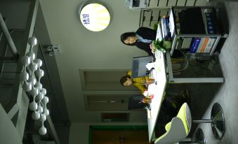 A couple is seated at an office table while two men stand behind the desk, and there is another woman present at Qiyou Capsule Youth Hostel