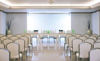 a large , empty conference room with rows of white chairs arranged in a semicircle around a long table at Mitsis Laguna Resort & Spa