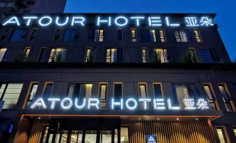 At night, there is a front view of a hotel and restaurant with a large sign on top at Atour Hotel