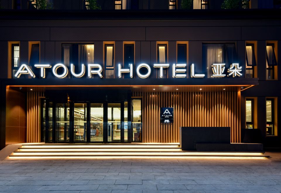 The hotel's front entrance is illuminated at night, displaying a welcoming sign above it at Atour Hotel