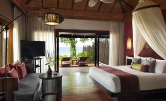 a spacious bedroom with a king - sized bed and a sliding glass door that leads to a balcony overlooking the ocean at Anantara Rasananda Koh Phangan Villas
