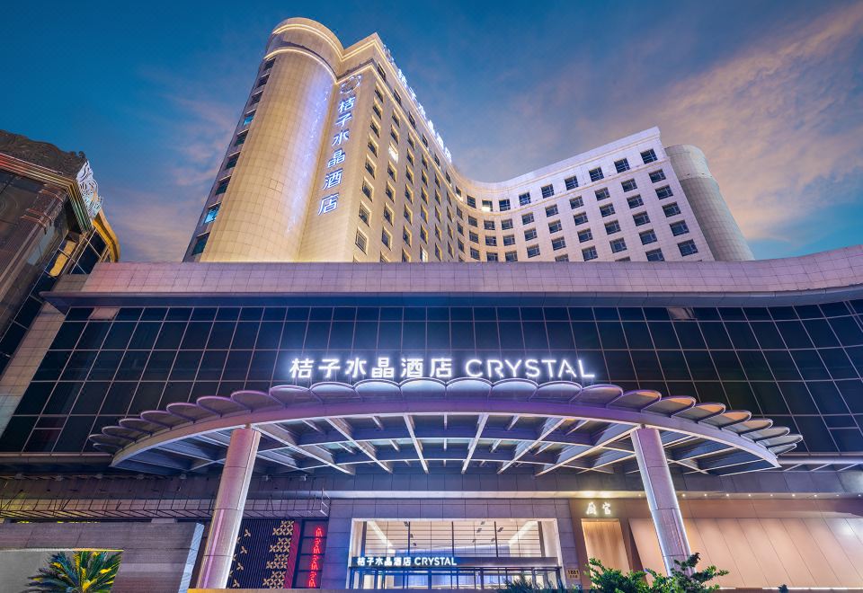 The front entrance of a hotel is located in an urban setting, surrounded by tall glass and steel buildings at Crystal Orange Hotel（Shanghai Hongqiao Gubei Road）