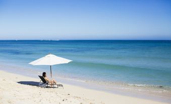 a woman is sitting on a beach chair under a white umbrella , enjoying the view of the ocean at Exmouth Escape Resort