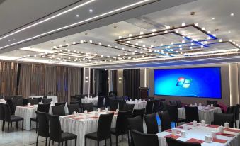 a large conference room with multiple tables and chairs , a screen displaying a windows logo , and multiple windows on the walls at Royal Hotel
