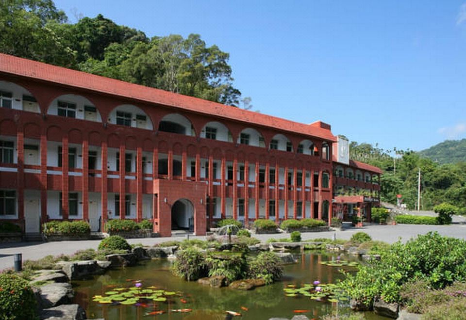 a red brick building with a pond in front of it , surrounded by lush greenery at Rainbow Hotel