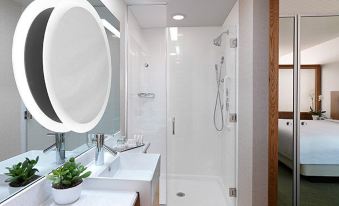 a modern bathroom with white tiles , a large mirror , and a walk - in shower area , along with a bed in the background at SpringHill Suites Columbia