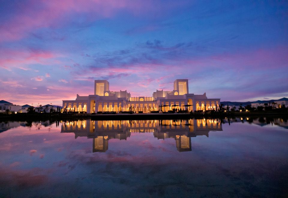a large white building with a reflecting pool in front of it , set against a beautiful sunset at Banyan Tree Tamouda Bay