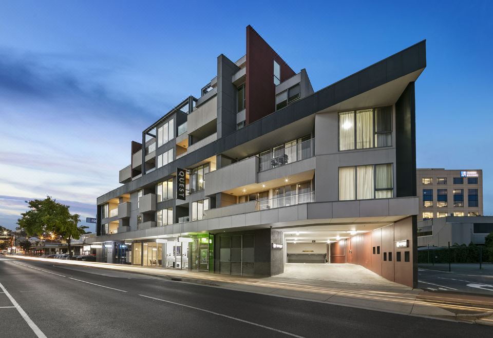 a modern building with multiple floors , balconies , and a parking lot in front of it at Quest Cheltenham