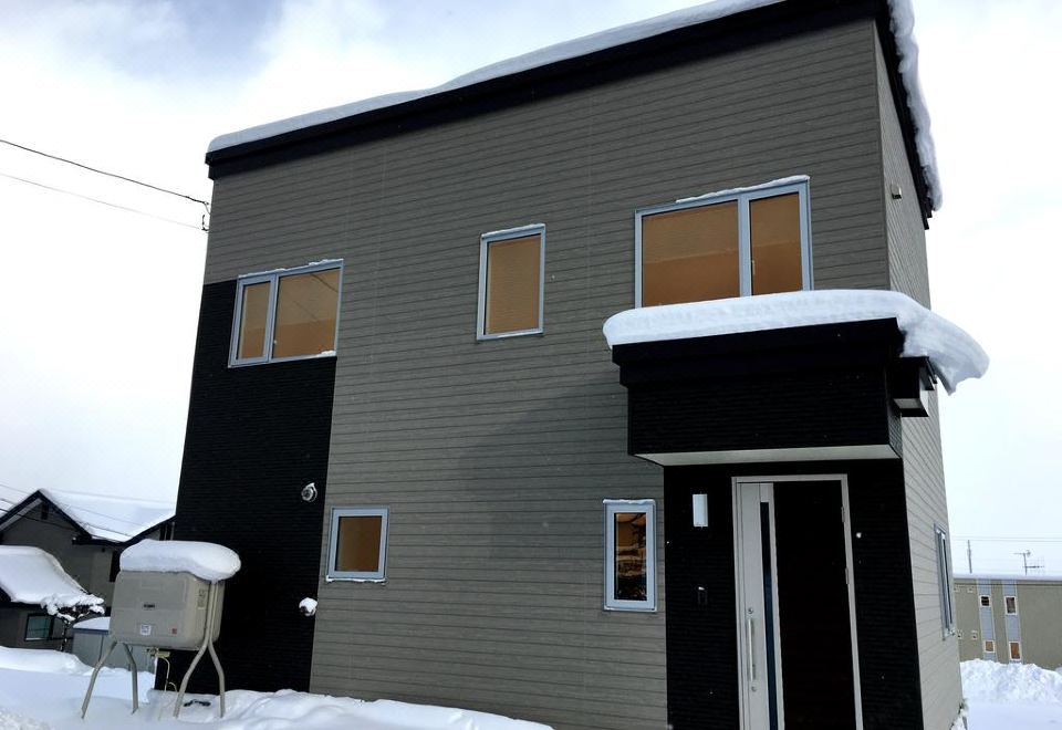a gray and black house with a black door is covered in snow , and the windows are closed at Ume