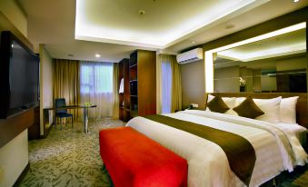 a large bed with a red bench in the middle of a room , surrounded by chairs at ASTON Pluit Hotel & Residence