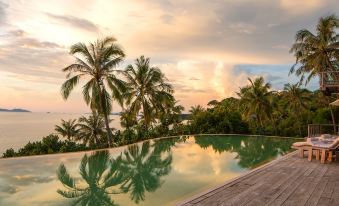 a large swimming pool surrounded by palm trees , with the sun setting in the background at Soneva Kiri