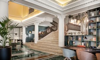 a grand lobby with a staircase leading to the second floor , a dining table , chairs , and potted plants at NH Madrid Nacional