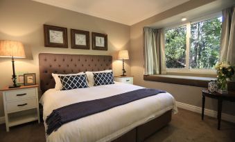 a cozy bedroom with a king - sized bed and a window overlooking a beautiful view at Parklands Country Gardens & Lodges Blue Mountains