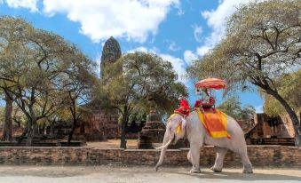 a man and a woman are riding an elephant in front of an old temple , with a blue sky and clouds in the background at Sala Ayutthaya