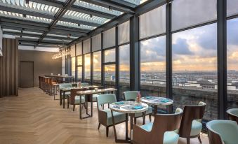 The restaurant features large windows and tables in the center, providing a view of the outdoors from the interior at Novotel Shanghai Clover
