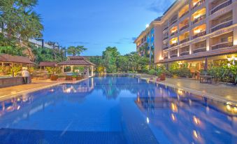 a large outdoor swimming pool surrounded by a hotel , with the sun setting in the background at Hotel Somadevi Angkor Resort & Spa