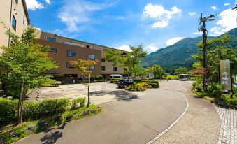 a large , beige building with a brown roof and greenery surrounding it , under a clear blue sky at Yufuin Hotel Shuhokan