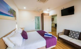 a large bed with a purple blanket and white sheets is in a room with wooden floors at Club Tropical Resort Darwin