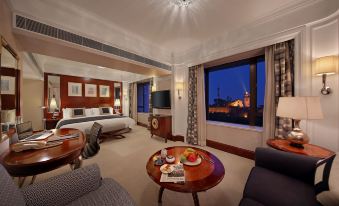 a luxurious hotel room with a king - sized bed , a dining table , and a large window overlooking the city at Hotel Royal