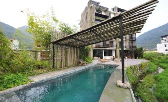 There is a swimming pool with an outdoor seating area and a wooden roof over the water in front at Yangshuo Sudder Street Guesthouse