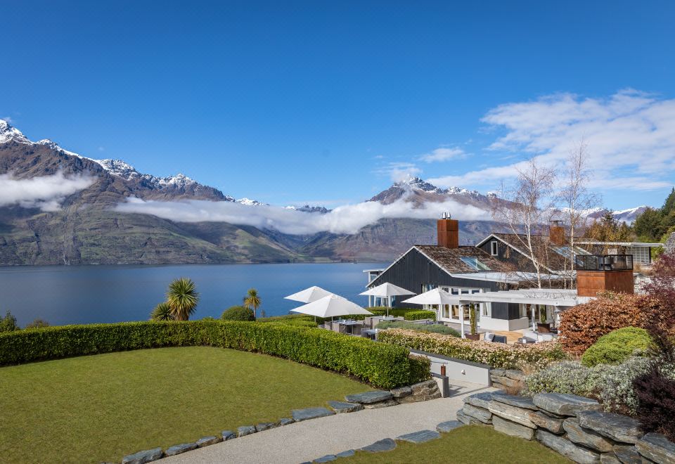 a beautiful house surrounded by lush greenery and a lake , with snow - capped mountains in the background at Rosewood Matakauri