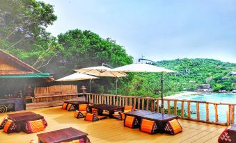 a wooden deck with several chairs and tables , umbrellas , and a view of trees and mountains in the background at Taatoh Seaview Resort