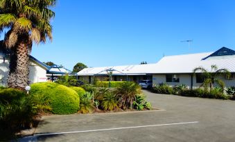a small white house surrounded by green grass and bushes , with a driveway leading up to it at Torquay Tropicana Motel