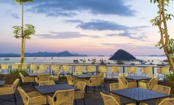 a large outdoor restaurant with yellow chairs and tables overlooking the ocean at sunset , creating a serene atmosphere at Meruorah Komodo Labuan Bajo